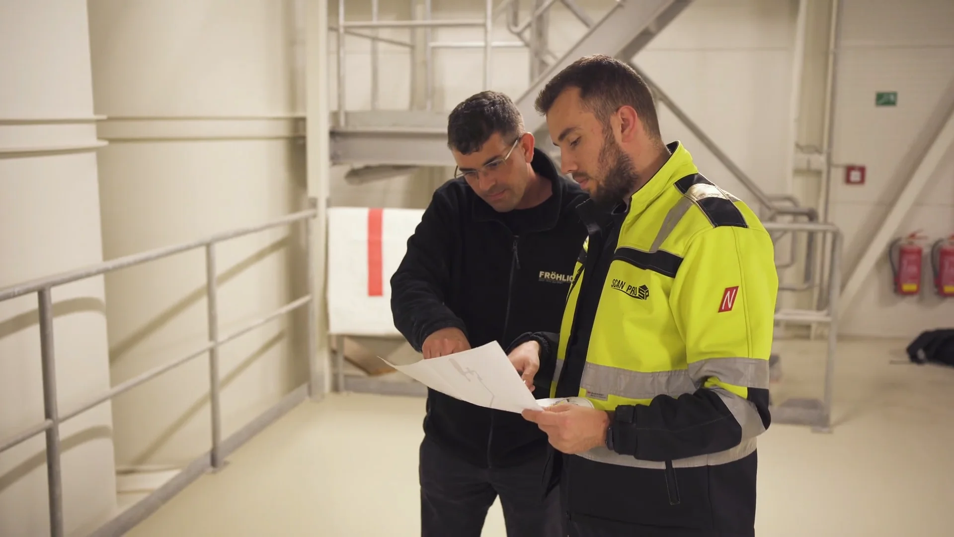 Two FRÖHLICH technicians reviewing a plant drawing on site in the hall